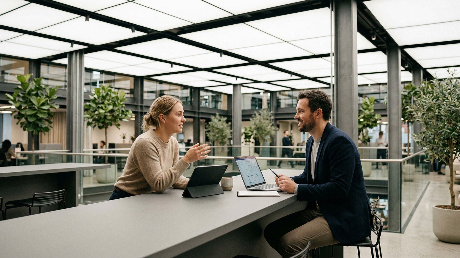 Two people sitting at a counter, discussing work with laptops in a modern office.